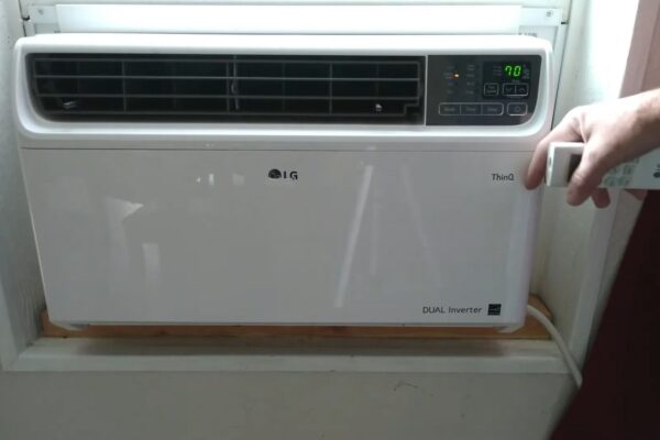 Alt tekst: LG inverter klima ugrađena u prozor sa daljinskim upravljačem u ruci korisnika.
