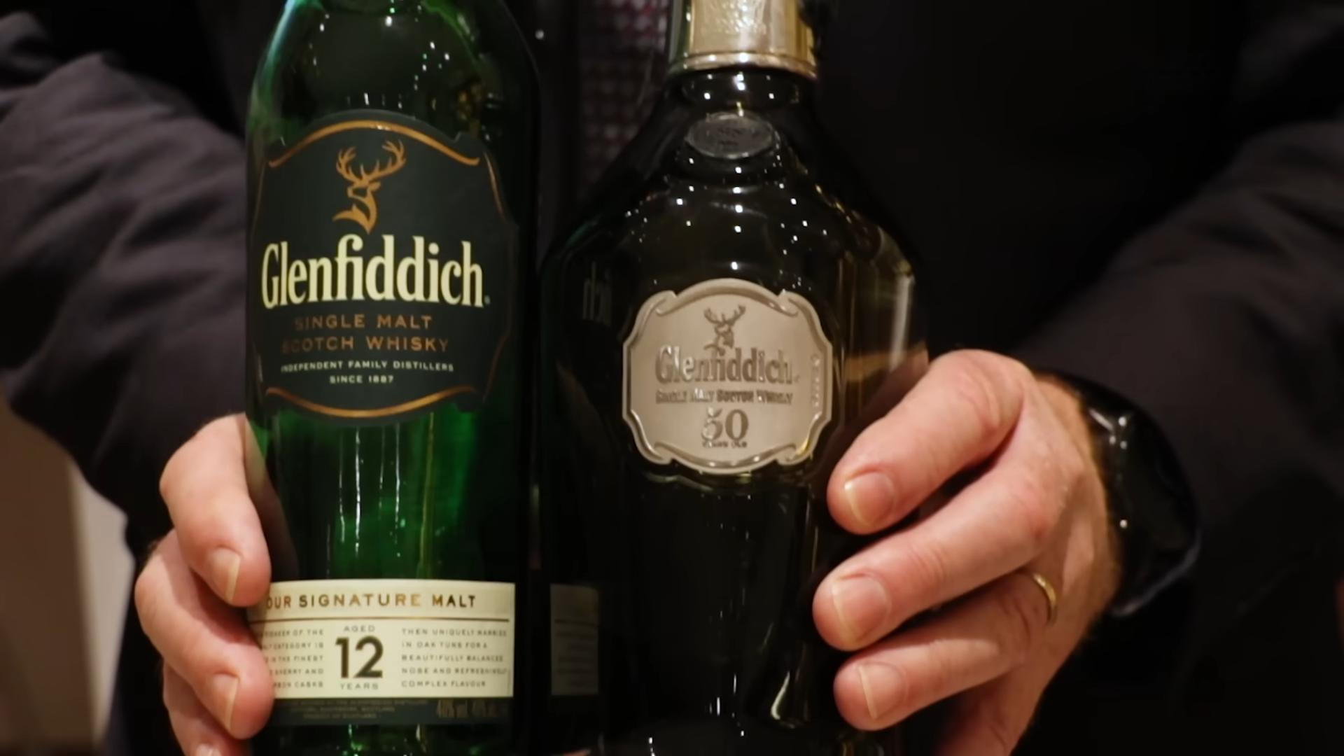Dve boce Glenfiddich viskija različitih godina odležavanja koje osoba drži u rukama.